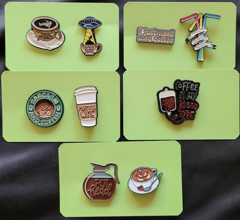 May include: Set of ten enamel pins with coffee themes. The pins feature images of coffee cups, coffee pots, and coffee-related sayings. The pins are on a green background.