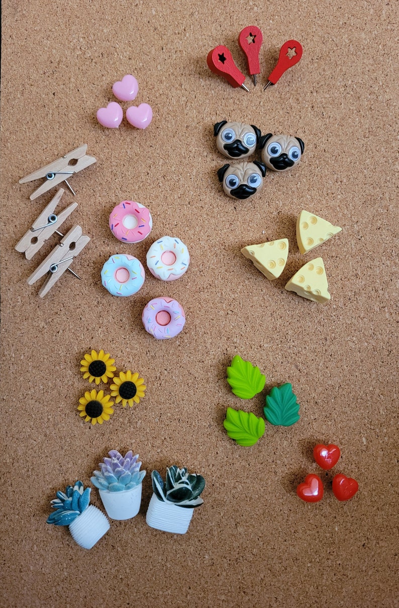 May include: A corkboard with various push pins, including donuts, hearts, pugs, cheese wedges, sunflowers, succulents, and leaves.