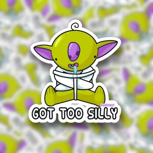 May include: A die-cut sticker featuring a cartoon green creature with large purple ears and a single purple eye, wearing a white straightjacket. The creature has a small blue drop of drool and the text GOT TOO SILLY printed in bold black letters.