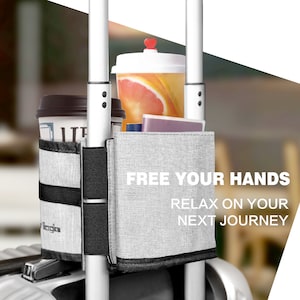 Puede incluir: Correa de equipaje gris con una correa negra y una bolsa de tela gris con el texto "FREE YOUR HANDS RELAX ON YOUR NEXT JOURNEY". La correa est&aacute; unida a un asa de equipaje plateada y sostiene dos tazas y un libro peque&ntilde;o.