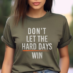 Puede incluir: Una camiseta verde con el texto "DON'T LET THE HARD DAYS WIN" en blanco con una l&iacute;nea naranja debajo de la palabra "WIN".