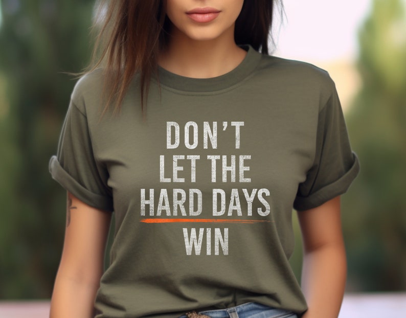 Puede incluir: Una camiseta verde con el texto "DON'T LET THE HARD DAYS WIN" en blanco con una l&iacute;nea naranja debajo de la palabra "WIN".