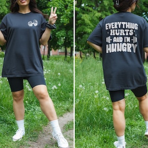 May include: Black oversized t-shirt with the text "Everything Hurts and I'm Hungry" printed on the back. The shirt is paired with black biker shorts.
