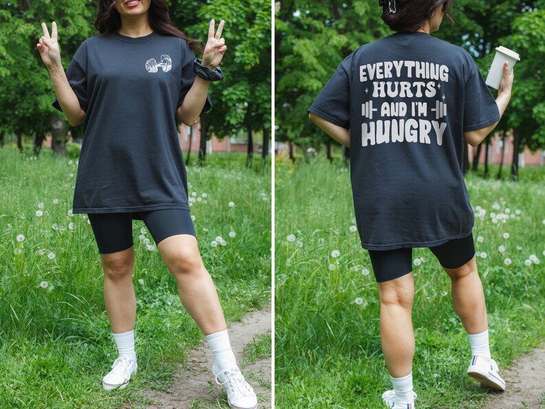 May include: Black oversized t-shirt with the text "Everything Hurts and I'm Hungry" printed on the back. The shirt is paired with black biker shorts.