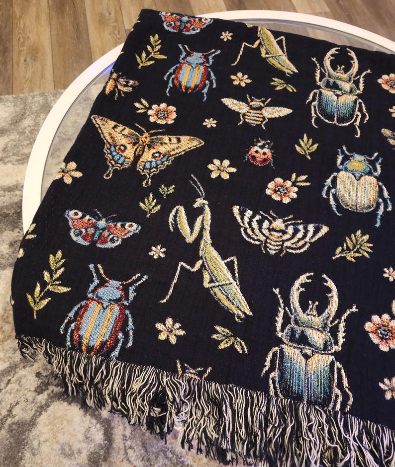May include: Black woven throw blanket with a repeating pattern of colorful butterflies, beetles, and praying mantises. The blanket has a fringe border.