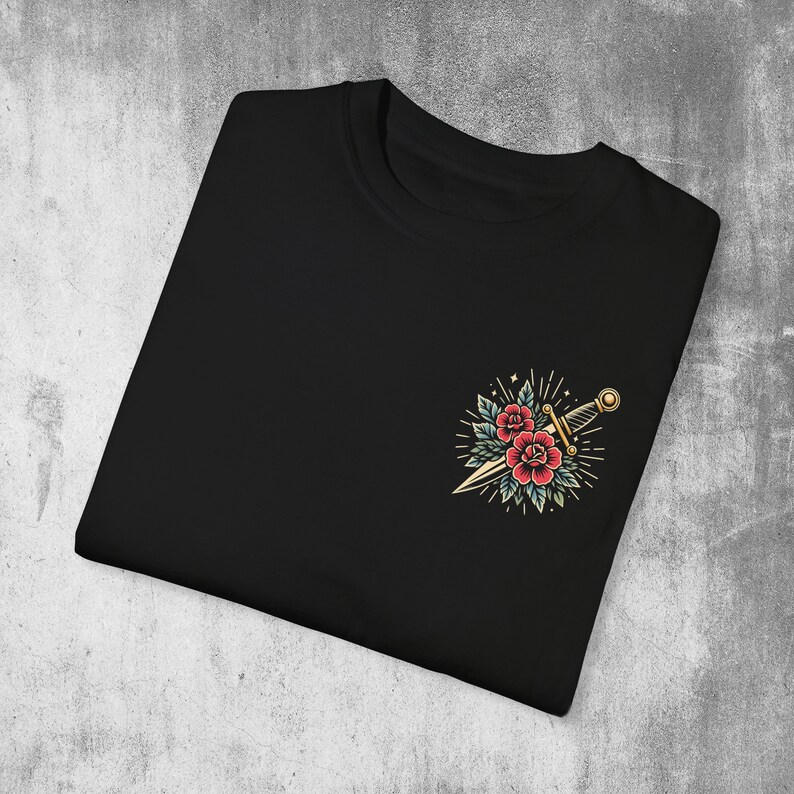 Puede incluir: Camiseta negra con un dise&ntilde;o bordado de estilo vintage de una daga y dos rosas rojas.