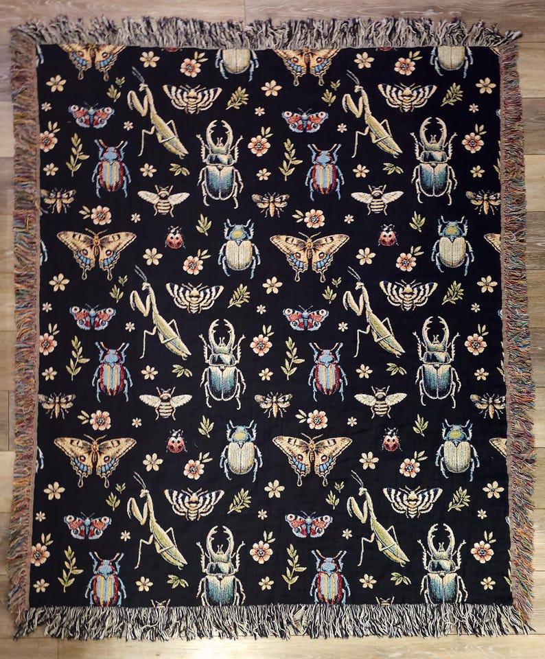 May include: Black woven throw blanket with a repeating pattern of butterflies, beetles, praying mantises, and flowers. The pattern is in shades of blue, green, red, and yellow.