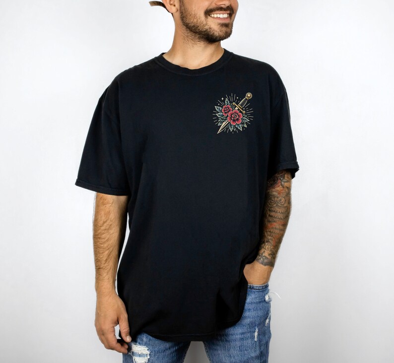 Puede incluir: Una camiseta negra con un gr&aacute;fico de una daga y flores. El gr&aacute;fico est&aacute; en un estilo vintage.