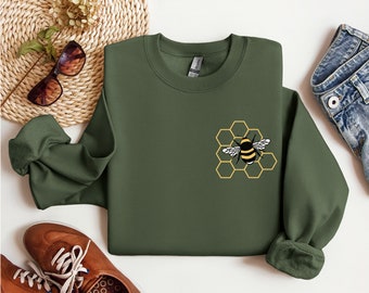 Könnte beinhalten: Ein grüner Pullover mit einem gelben und schwarzen Bienen-Motiv auf einem Wabenmuster.
