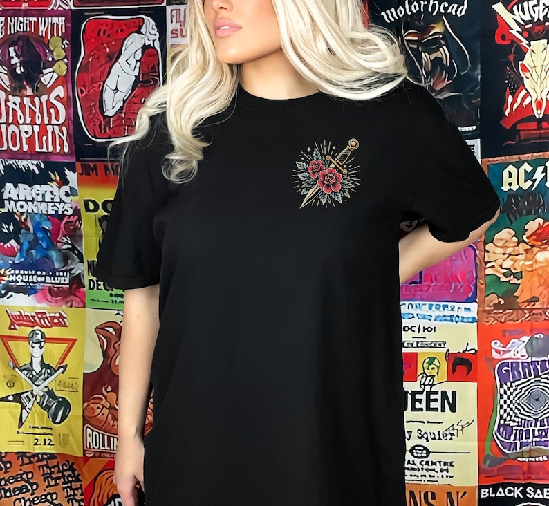 Puede incluir: Camiseta negra con un tatuaje de estilo vintage de una daga y flores en el pecho izquierdo.