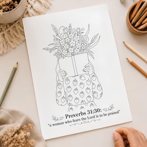 Puede incluir: Una página para colorear blanca con una ilustración de líneas de una figura que sostiene un libro con un gran ramo de flores que emerge de la parte superior. La figura lleva un suéter con estampado de fresas. El texto dice: Proverbs 31:30: a woman who fears the Lord is to be praised.