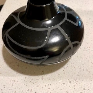 May include: Black pottery vase with a geometric design. The vase has a wide base and a narrow neck.