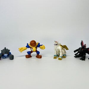 Peut inclure: Ensemble de figurines et un dé. Les figurines comprennent une créature épineuse bleue et grise, un guerrier marron et jaune, un lion ailé blanc et une figurine noire en forme d'insecte avec des ailes rouges.
