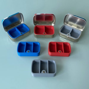 May include: Five small, rectangular containers with lids. Three containers are silver with blue, red, and gray silicone inserts. Two containers are blue and red silicone.