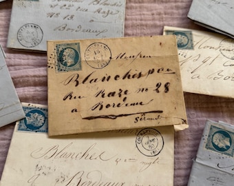 May include: A collection of antique envelopes in various shades of cream and light blue, scattered on a pink surface. The envelopes feature handwritten script, stamps, and postmarks. Some envelopes have the text "Bordeaux" and "Blanches".