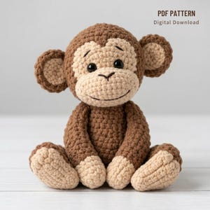 Può includere: Una bambola a forma di scimmia all'uncinetto nei toni del marrone e del beige. L'animale di peluche fatto a mano ha un viso sorridente, grandi orecchie ed è seduto con le gambe distese. Il testo "PDF PATTERN Digital Download" è visibile.