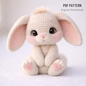 May include: A crocheted bunny with large, dark eyes, pink cheeks, and long ears with pink inner ears. The bunny is sitting with its paws together and has a small, fluffy tuft of hair on its head. The text "PDF PATTERN Digital Download" is in the upper right corner.