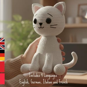 Può includere: Una bambola a forma di gatto bianco fatta a mano all'uncinetto, con occhi neri e baffi. Il gatto ha accenti rosa all'interno delle orecchie. L'immagine include il testo "Includes 4 Languages English, German, Italian and French."