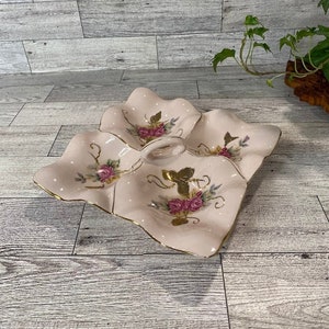May include: A white ceramic serving dish with a gold trim and floral design. The dish has four sections and a handle in the center.