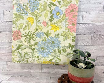 Peut inclure: Un morceau de tissu rectangulaire avec un motif floral composé de fleurs jaunes, bleu clair et roses sur un fond crème. Un petit pot en céramique vert et rouge contenant une plante grasse repose sur un socle en bois sculpté.