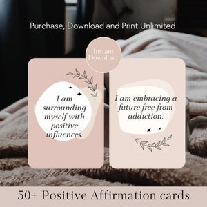 May include: Two pink affirmation cards with black text and illustrations of leaves. The card on the left reads "I am surrounding myself with positive influences." The card on the right reads "I am embracing a future free from addiction." The cards are on a brown fuzzy surface. 50+ Positive Affirmation cards.