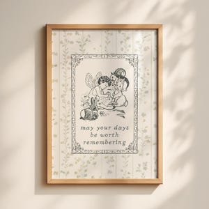 May include: A framed wall art print featuring a light beige background with a subtle vertical floral pattern. The central illustration depicts a fairy with wings sitting among small animals, with the text "may your days be worth remembering" below.