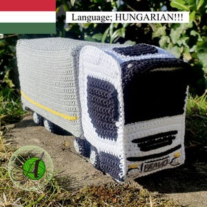 Puede incluir: Un camión de juguete de crochet con una cabina blanca y un remolque gris. El camión tiene detalles negros y las palabras "BRAVO" en la parte delantera. El camión está sentado en una superficie marrón.