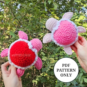 May include: Two handmade crochet turtle toys. One turtle has a red shell with a white border, and the other has a pink shell with a white border. Both turtles have pink flippers and heads. The text "PDF PATTERN ONLY" is in a white circle.