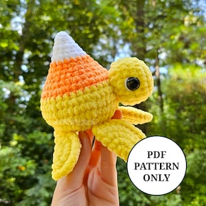 May include: Crocheted amigurumi sea turtle toy with a candy corn design. The turtle is yellow and orange with white accents. The toy is being held in a hand. The image includes the text "PDF PATTERN ONLY".