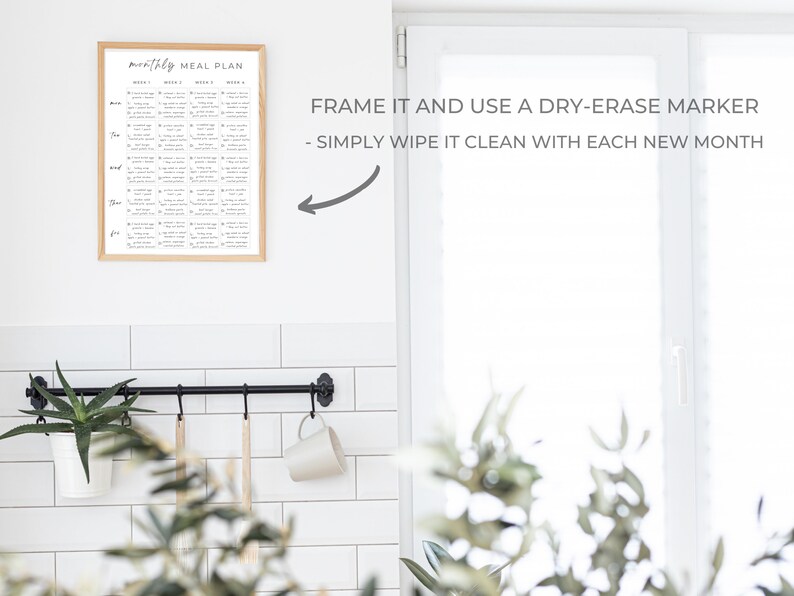 May include: A framed monthly meal planner with a white background and black text. The text says "monthly meal plan" and lists the days of the week and weeks of the month. The image is in a white kitchen with a black metal rack and a plant hanging from it. The text below the image says "FRAME IT AND USE A DRY-ERASE MARKER - SIMPLY WIPE IT CLEAN WITH EACH NEW MONTH".