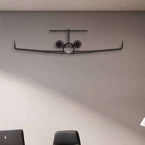 Puede incluir: Una obra de arte mural de metal negro que representa un avión. La obra de arte representa un contorno detallado de un avión, incluyendo alas, fuselaje y motores. El arte está montado en una pared gris claro en un entorno de oficina.