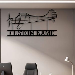Puede incluir: Arte de pared de avión de metal negro con una hélice y el texto "CUSTOM NAME". La obra de arte está montada en una pared gris claro en un entorno de oficina. El diseño del avión es un contorno detallado.
