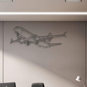 May include: A black metal airplane wall art piece. The artwork shows a detailed outline of a commercial jet in flight, mounted on a neutral-coloured wall. The office setting includes a desk, chair, and computer.
