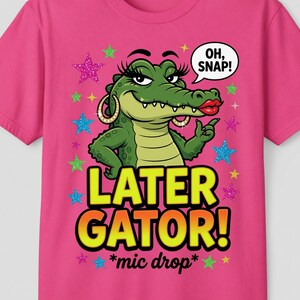 Puede incluir: Una camiseta rosa brillante con un cocodrilo de dibujos animados con maquillaje y pendientes de aro. El texto dice "LATER GATOR!" y "*mic drop*". Un bocadillo dice "OH, SNAP!". El diseño incluye estrellas de varios colores.