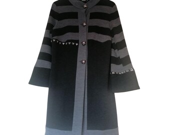 May include: A long-sleeved, striped, black and gray cardigan with a button closure. The cardigan has a unique design with a black and gray panel on the front and a silver beaded trim on the sleeves.