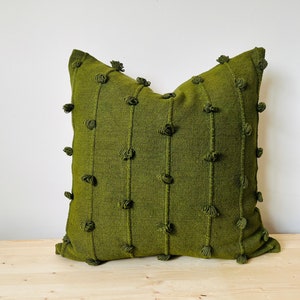 以下が含まれることがあります： テクスチャのある生地と装飾的なポンポンが付いた緑色のクッション