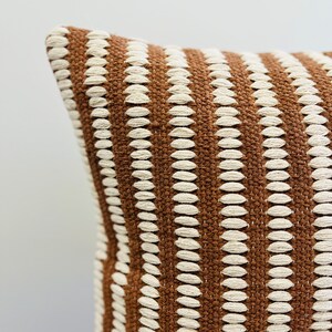 May include: Brown and white striped throw pillow with a textured woven design.