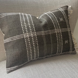 May include: Black and white patterned throw pillow with a woven texture. The pillow is rectangular and has a fringe trim.