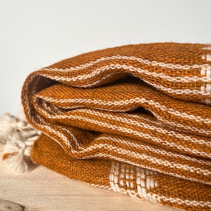 May include: A folded brown throw blanket with white stripes. The blanket has a fringe on one end.