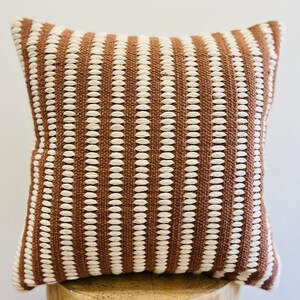 May include: A brown and white striped throw pillow with a textured woven design.