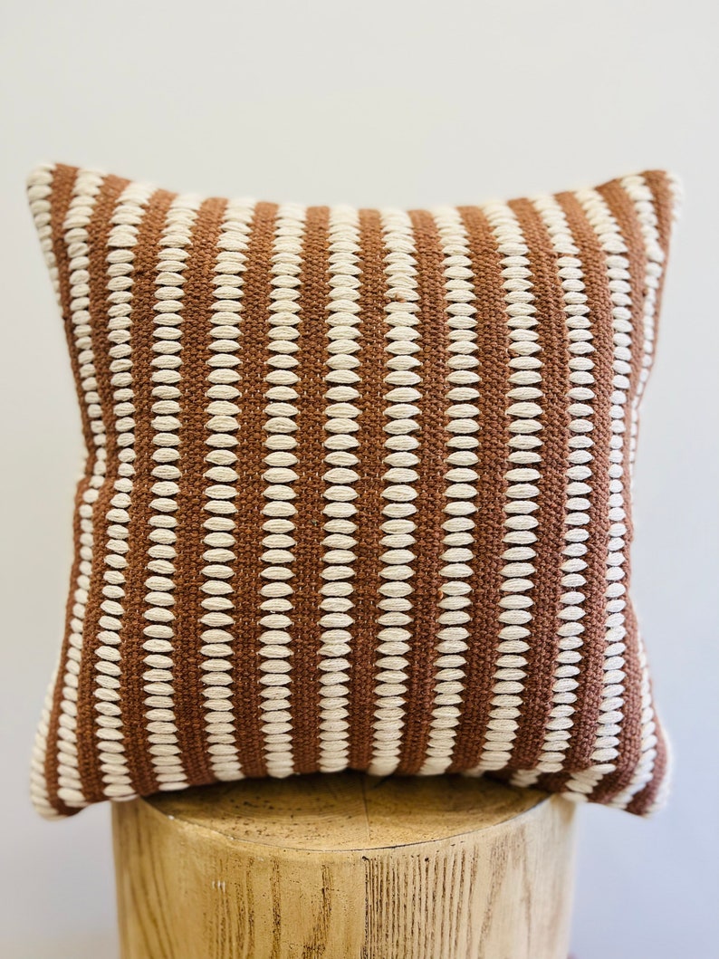 May include: A brown and white striped throw pillow with a textured woven design.