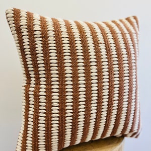 May include: A brown and white striped throw pillow with a textured woven design.