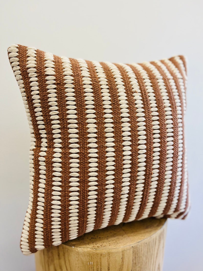 May include: A brown and white striped throw pillow with a textured woven design.