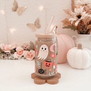 K&ouml;nnte beinhalten: Ein durchsichtiger Glasbecher mit Bambusdeckel und Strohhalm, verziert mit Halloween-Stickern, darunter ein Geist, eine Spinne und ein K&uuml;rbislaterne. Der Becher steht auf einem bl&uuml;tenf&ouml;rmigen Untersetzer aus Kork.