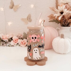 K&ouml;nnte beinhalten: Ein durchsichtiger Glasbecher mit Bambusdeckel und Strohhalm, verziert mit Halloween-Aufklebern. Die Aufkleber zeigen einen rosa Totenkopf, eine schwarze Katze, einen Geist und S&uuml;&szlig;igkeiten. Der Becher steht auf einem Untersetzer aus Kork.