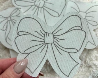 May include: Set of six white fabric stick and stitch bow patterns. The bows are outlined in gray.