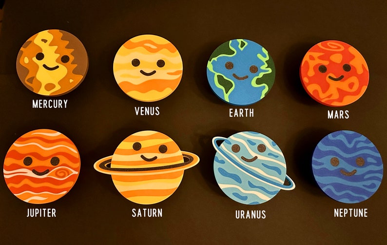 May include: Eight planet-shaped coasters with smiling faces and planet names: Mercury, Venus, Earth, Mars, Jupiter, Saturn, Uranus, and Neptune. The coasters are arranged on a black surface, ideal for space enthusiasts.
