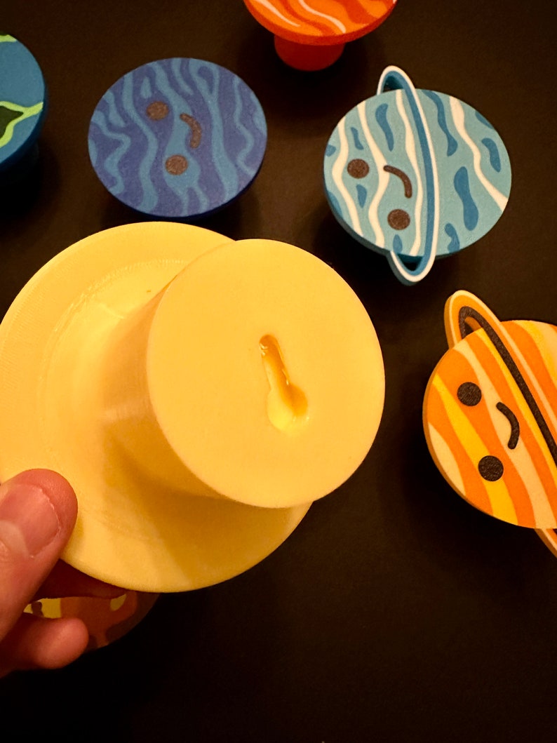 May include: A selection of planet-shaped magnets with smiling faces. The designs include blue and white stripes, orange and white stripes, and blue swirls. A yellow magnet with a keyhole shape is also visible. The magnets are for decorative purposes.