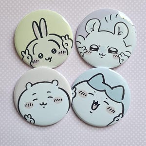 May include: Four circular pin-back buttons featuring cartoon characters. The top left is a pale yellow rabbit, the top right is a light purple bear, the bottom left is a light blue bear, and the bottom right is a light blue bear with a bow.
