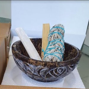 May include: A brown, carved bowl containing a white sage smudge stick, a white cleansing stick, and a wooden stick.